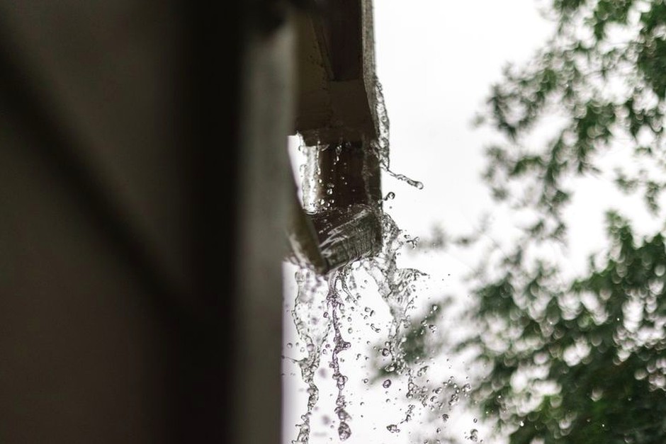 Rainwater spilling from a roof edge during a wet afternoon.